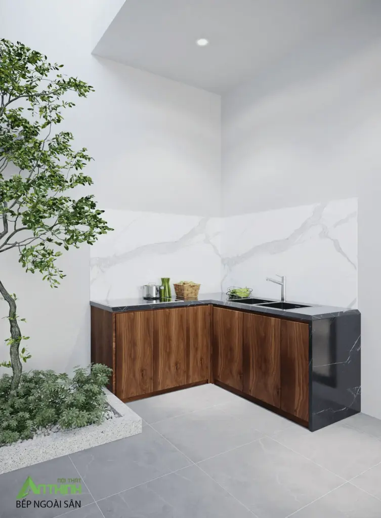 Bếp ngoài sân – tủ dưới gỗ óc chó chữ L, mặt bàn đá đen, ốp lưng marble trắng, cây xanh tự nhiên trồng sát bên tạo không gian nấu nướng ngoài trời lý tưởng
