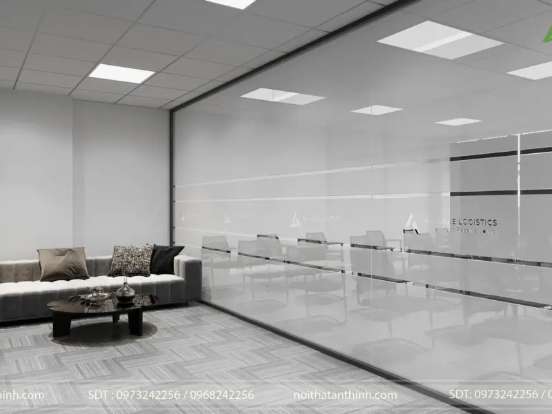 Khu chờ tiếp khách – bộ sofa xám đệm rút, bàn trà tròn thấp, vách kính lớn in dải logo nhìn thông sang phòng đào tạo, không gian sáng sủa