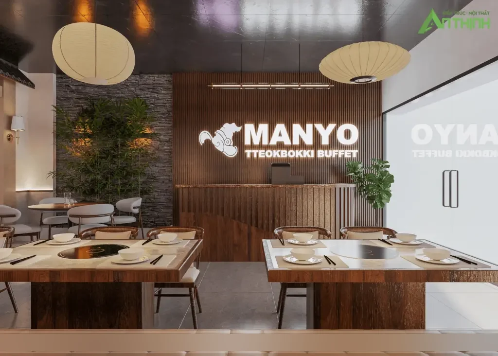 Quầy lễ tân ấn tượng – logo MANYO LED nổi trên vách lam gỗ, đèn lồng giấy lớn, mảng đá tự nhiên trồng tre xanh, dãy bàn lẩu gỗ phía trước