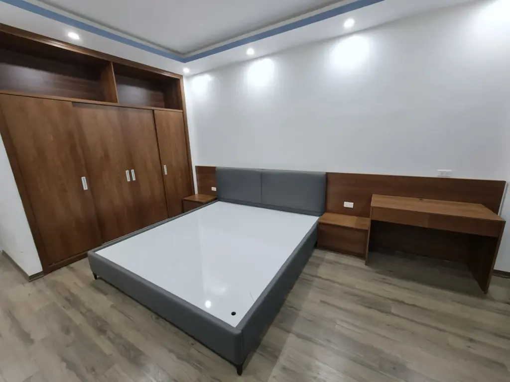 Ảnh thực tế – phòng ngủ giường bọc nệm xám, tủ áo và bàn làm việc vân gỗ nâu
