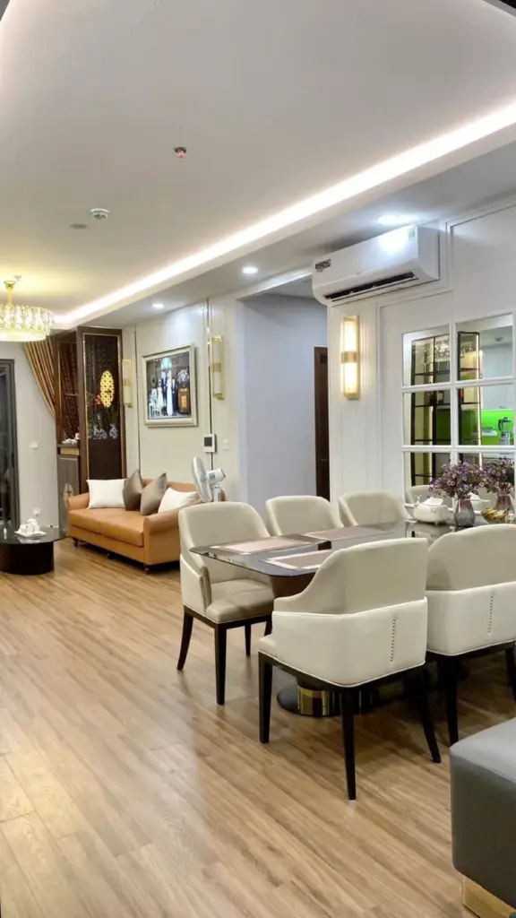 Bàn ăn 6 ghế bọc nỉ kem cạnh sofa da cam, đèn tường vàng và tranh treo tường