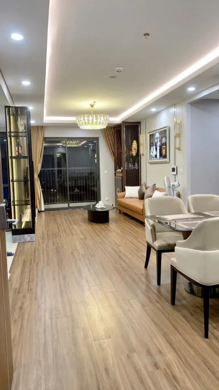 Phòng khách – phòng ăn liên thông, trần giật cấp LED hắt viền, đèn chùm pha lê, sàn gỗ vân sáng nối ra ban công