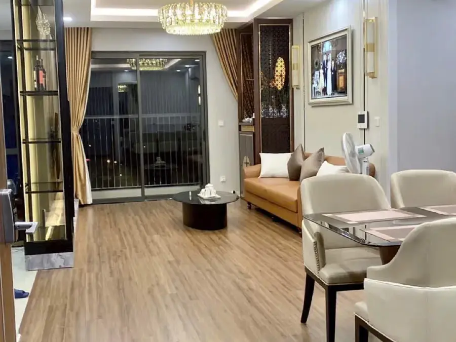 Phòng khách – phòng ăn liên thông, trần giật cấp LED hắt viền, đèn chùm pha lê, sàn gỗ vân sáng nối ra ban công