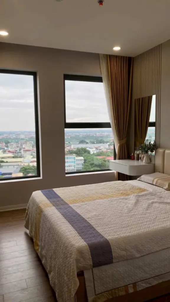 Phòng ngủ master góc nhìn khác – bàn trang điểm treo tường, vách lam gỗ dọc, rèm be hai lớp
