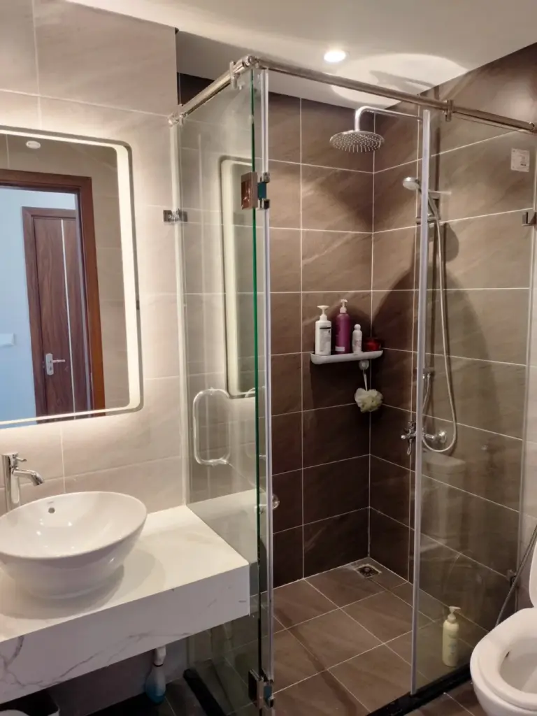 Phòng tắm – vách kính cường lực, gạch giả đá nâu xám, lavabo bàn đá trắng, gương LED