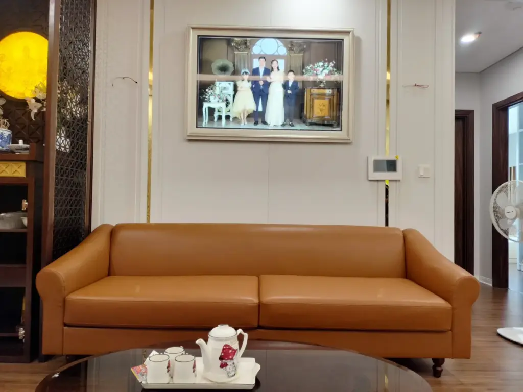 Sofa da màu cam cognac trên nền tường trắng nẹp kim loại vàng, bàn trà mặt kính