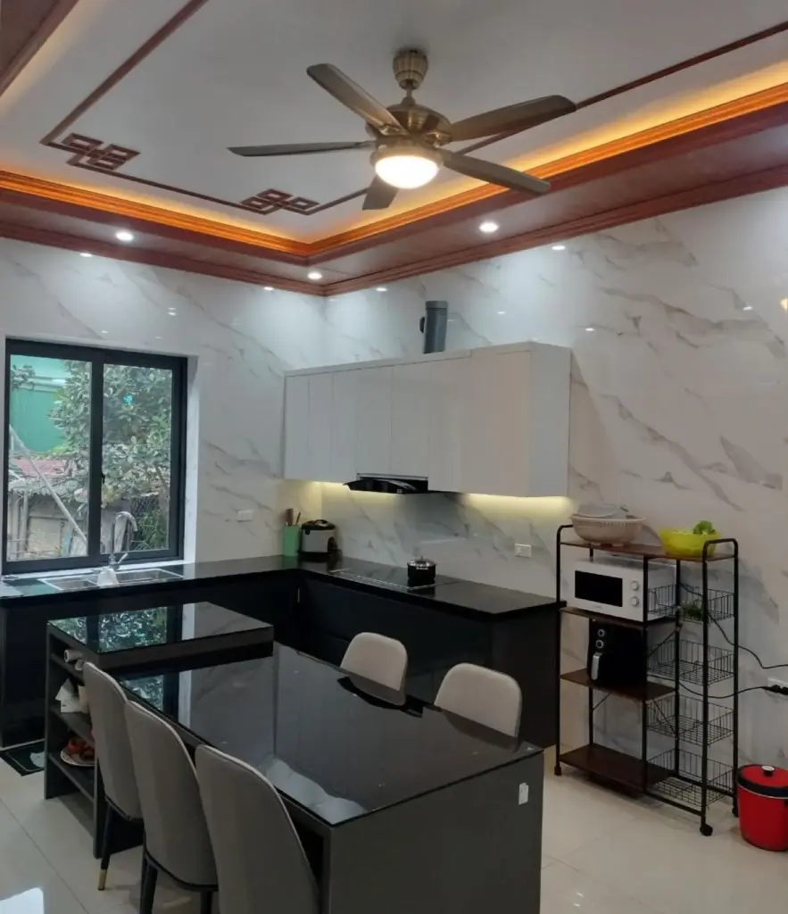 Ảnh thực tế – bếp chữ L tủ trên trắng tủ dưới đen, bàn ăn đá đen, trần viền gỗ