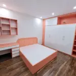 Ảnh thực tế – phòng bé gái hồng đào: giường đầu bo tròn, tủ áo cánh trắng kịch trần, kệ mở dọc, bàn học và kệ treo
