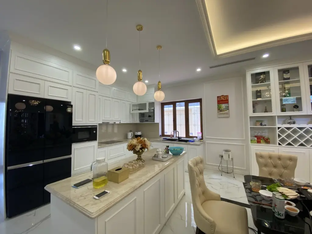 Ảnh thực tế – bếp trắng cánh phào chỉ, đảo bếp mặt đá, đèn thả quả cầu