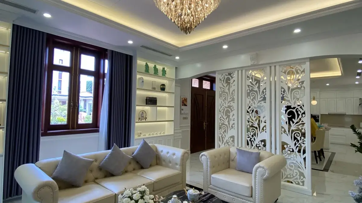 Ảnh thực tế – phòng khách sofa da kem, vách CNC hoa văn trắng, đèn chùm pha lê