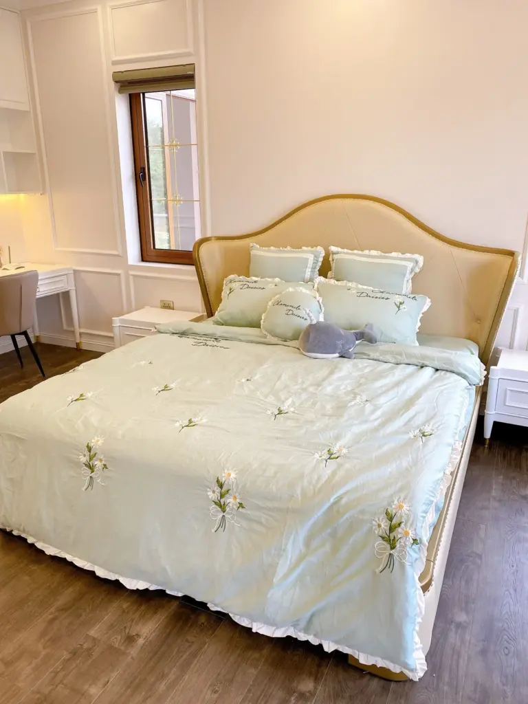 Ảnh thực tế – phòng ngủ đầu giường bọc nệm bo cong viền vàng, tường phào chỉ
