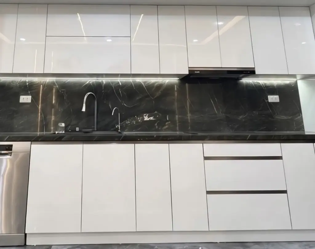 Ảnh thực tế – tủ bếp thùng inox 304, cánh acrylic trắng bóng gương, tủ trên hai tầng kịch trần, tường ốp vân đá đen