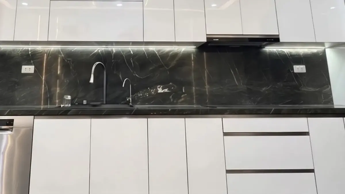 Ảnh thực tế – tủ bếp thùng inox 304, cánh acrylic trắng bóng gương, tủ trên hai tầng kịch trần, tường ốp vân đá đen