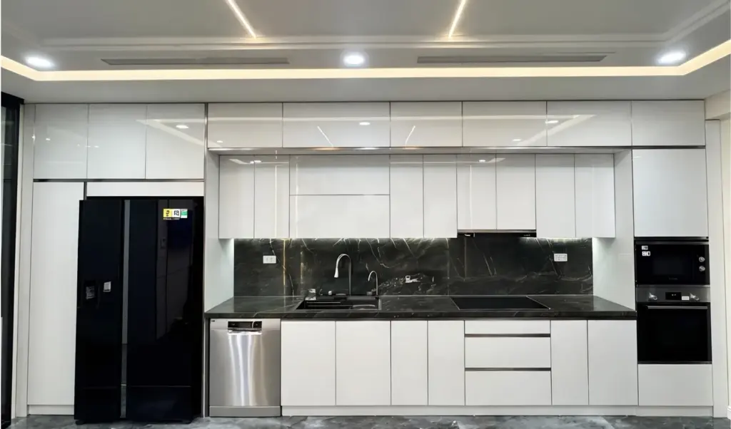 Ảnh thực tế – toàn cảnh dãy bếp inox 304 cánh nhựa phủ Acrylic trắng, tủ lạnh và máy rửa bát âm tủ, tường đá đen
