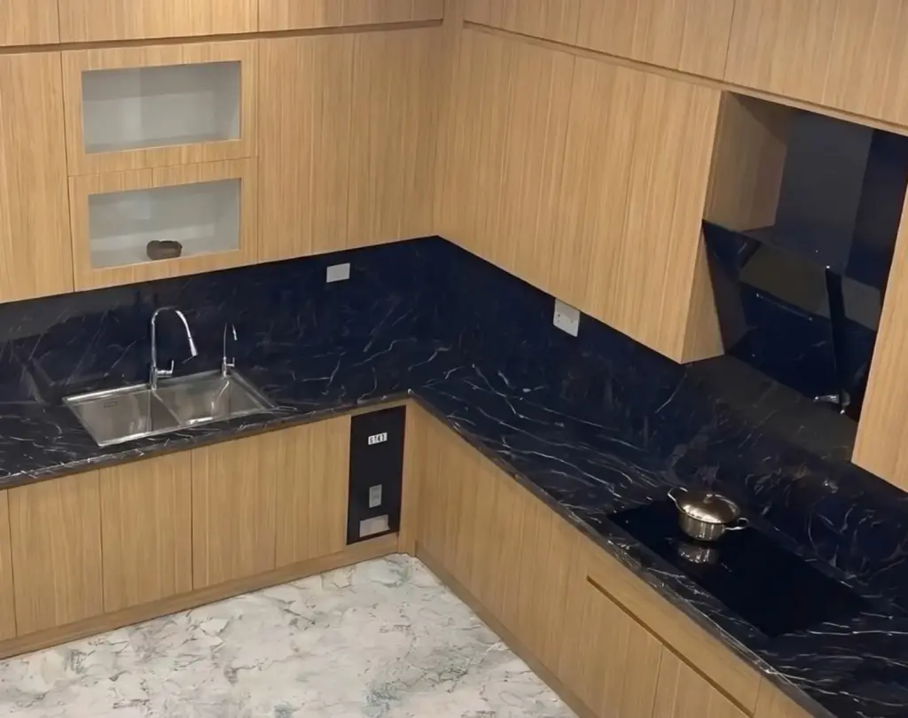 Ảnh thực tế – tủ bếp inox 304 chữ L cánh Melamine màu gỗ sáng, tường và mặt bếp tông đen vân