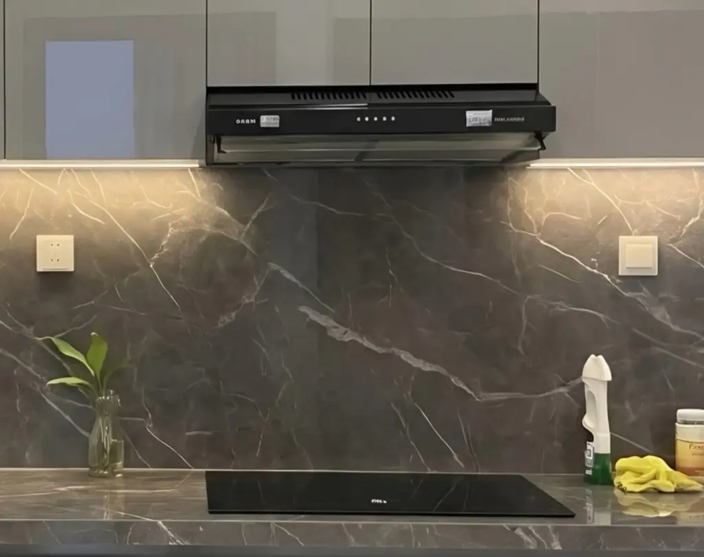 Ảnh thực tế – bếp từ âm kính đen, máy hút mùi đen dưới tủ trên, tường ốp đá xám vân trắng