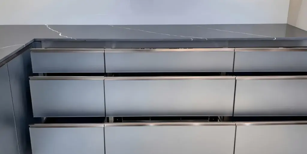 Ảnh thực tế – ba tầng ngăn kéo tủ dưới cánh kính nhám viền inox mảnh, mặt đá xám